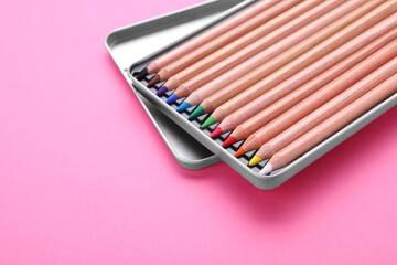 Box with many colorful pastel pencils on pink background, closeup and space for text. Drawing supplies
