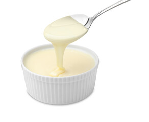 Condensed milk flowing down from spoon into bowl isolated on white