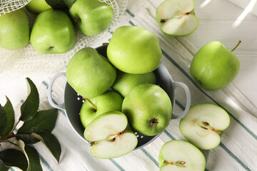 Fresh green apples with water drops and leaves on white wooden table, flat lay