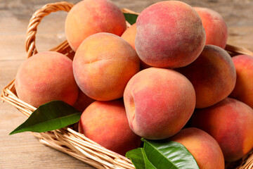 Fresh peaches and leaves in basket on wooden table, closeup