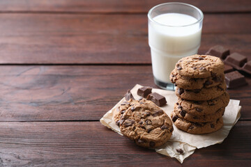 Delicious chocolate chip cookies and glass of milk on wooden table, space for text