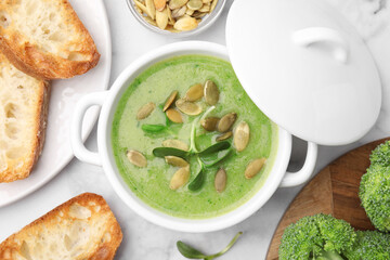 Delicious broccoli cream soup with pumpkin seeds on white marble table, flat lay