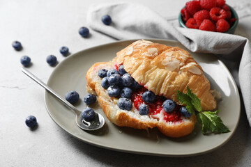 Delicious croissant with berries, almond flakes and spoon on light grey table