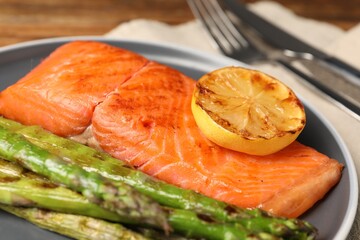 Tasty grilled salmon with asparagus and lemon served on plate, closeup