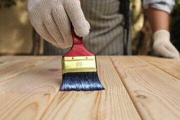 Man varnishing wooden surface with brush outdoors, closeup