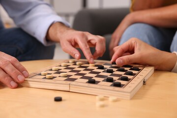 People playing checkers at wooden table indoors, closeup