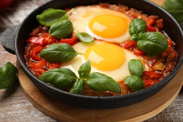 Delicious Shakshuka with basil on wooden table, closeup
