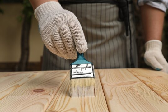 Man varnishing wooden surface with brush outdoors, closeup