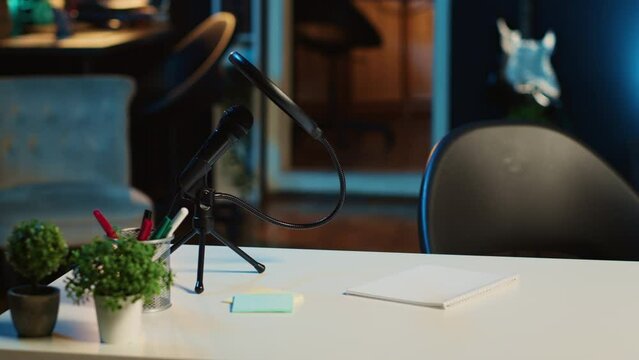 Close up shot of coffee table with professional microphone and mini house plants in dimly lit empty home studio interior. Streaming recording equipment in living room illuminated by RGB lights