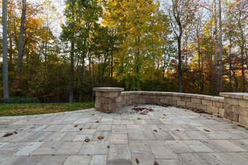 Picturesque backyard view in autumn season with patio pavers and stone wall, autumn leaves, and...