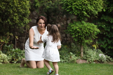 Cute baby girl making first steps on green grass in park. Mother and her little daughter spending time together