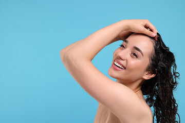 Beautiful happy woman washing hair on light blue background. Space for text