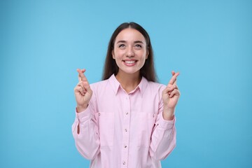 Happy woman crossing her fingers on light blue background