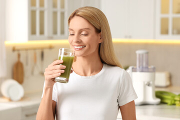 Happy woman with glass of fresh celery juice in kitchen