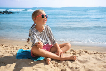 Happy little girl in stylish sunglasses on sandy beach near sea