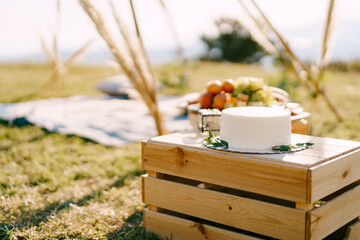 Wedding cake on a plate stands on a wooden box on a lawn