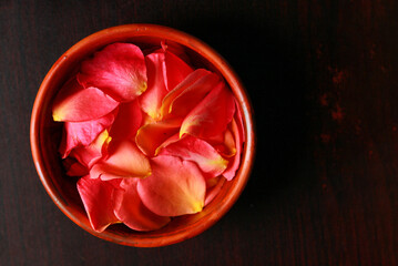 Rose petals in a bowl on a dark wooden background.