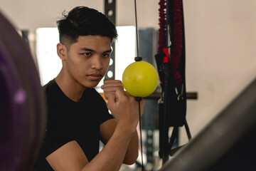 A young asian man training his punching reflexes and hand -eye coordination on a yellow double end bag. Boxing practice at the gym.