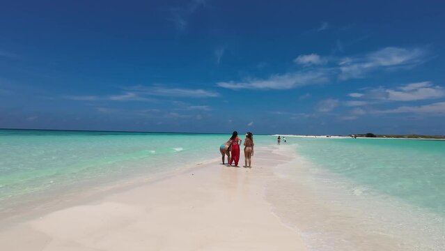 three latin women friends stand on sandbank chatting and have fun vacations on tropical beach.