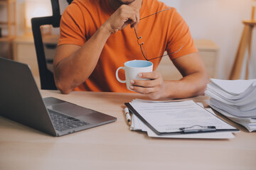 Satisfied caucasian successful guy, freelancer or ceo, relaxes at workplace with legs thrown on table. Stylish guy uses laptop, browses the Internet, looks for ideas for a project, sitting at the desk