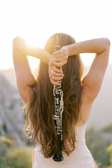 Girl-musician with a flute in her hands behind her back stands in the mountains. Back view