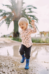 Smiling little girl in rubber boots jumping on a puddle