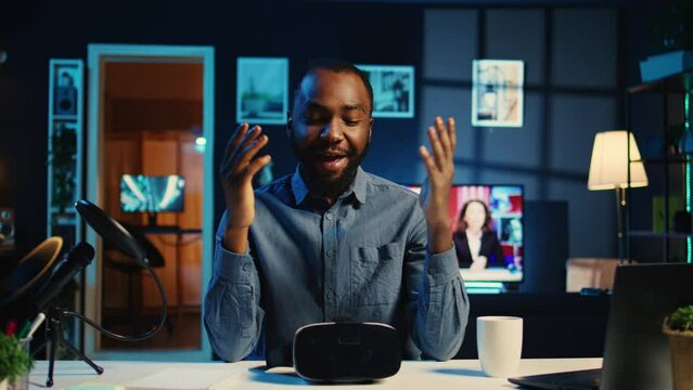 Tech content creator filming unboxing of newly released gaming VR glasses for audience in neon illuminated home studio. BIPOC internet star offers virtual reality headset recommendation to subscribers