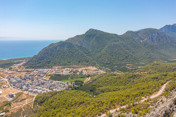 Fototapeta na wymiar Flight over ridge mountain pass rocky terrain with bushes, bird's eye view overlooking the city, houses and buildings, roads and ships, Mediterranean coast, resort area, vacation trip.