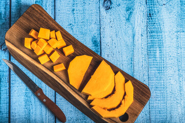 Pumpkin slices on a cutting board and half a pumpkin on a wooden blue background. Traditional autumn food