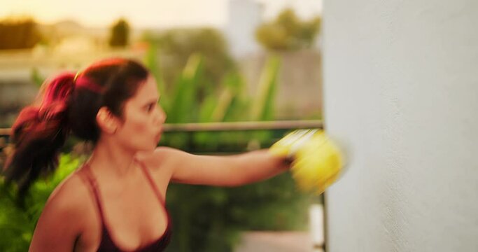 Indian asian angry sporty young woman lady ido self sport class punch on wall at outdoor home athletic boxer adult hindu female girl standing in boxing gloves learn exercise beating warm up at house