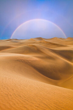 desert landscape with dunes and a rainbow on the horizon