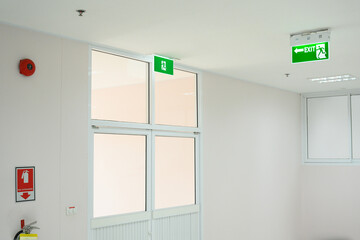 Selective fire exit sign on white ceiling and glass door.Green fire escape sign hang on the ceiling in the office.Fire fighting equipment concept.
