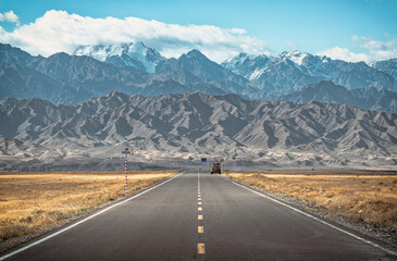 The view of a straight highway going towards the snow capped mountains in regional area in Xinjiang - obrazy, fototapety, plakaty