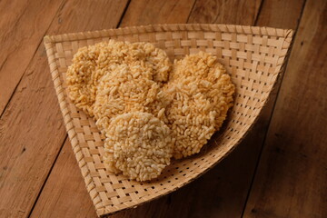 Rengginang is a typical Indonesian snack made from glutinous rice grains that are seasoned and fried. Served on a bamboo besek on a wooden table. Indonesian food. Camilan gurih. Rengginang goreng. 