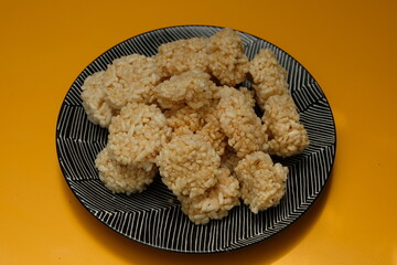 Rengginang is a typical Indonesian snack made from glutinous rice grains that are seasoned and fried. Served on a black plate  on yellow table. Indonesian food. Camilan gurih.