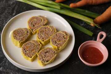 Rolade Daging Sapi. Beef roulade on a white ceramic plate. Made from ground beef, pepper, nutmeg, eggs, garlic, carrot, onion leaves. Served with tomato sauce.