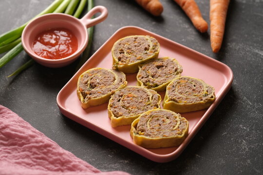 Rolade Daging Sapi. Beef roulade on a square pink ceramic plate. Made from ground beef, pepper, nutmeg, eggs, garlic, carrot, onion leaves. Served with tomato sauce.