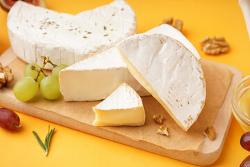 Wooden board with pieces of tasty Camembert cheese on yellow background