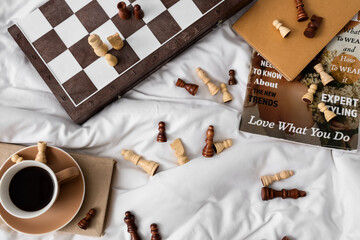 Chess pieces with cup of coffee and magazine on bed, top view