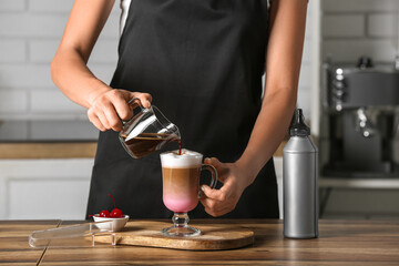 Fototapeta na wymiar Female barista preparing tasty coffee on wooden table in kitchen
