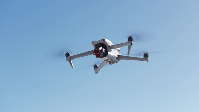 Modern white drone hovering with blue clear sky for copy space in background. Low angle view