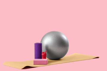 Fitness ball, foam roller, yoga block and mat on pink background
