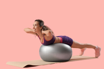 Beautiful adult woman exercising on fitness ball against pink background