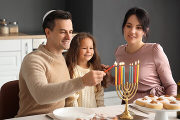 Happy family lighting candles for Hanukkah in kitchen