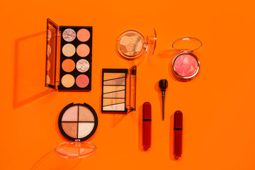 Beautiful palettes of eyeshadows and different decorative cosmetics on orange background