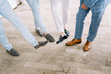Groom and groomsmen show off their shoes with outstretched feet. Cropped. Faceless