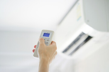 Man's hand using remote control open The air conditioner is cooled to 25 degrees Celsius in his bedroom. Health concepts and energy savings
