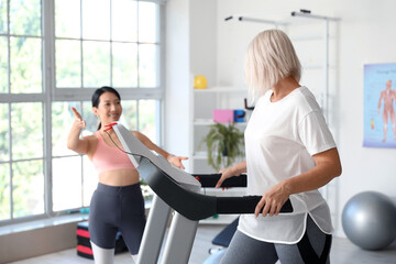 Fototapeta na wymiar Mature woman training with therapist on treadmill in rehabilitation center