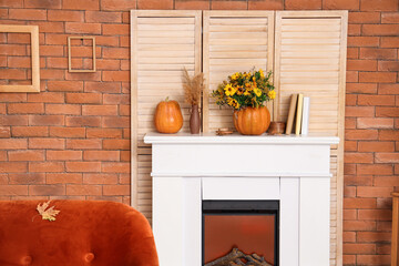Pumpkins with flowers, books and fallen leaves on fireplace in living room