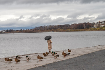 The woman with umbrella on the city embankment in the autumn park. Rainy overcast weather.